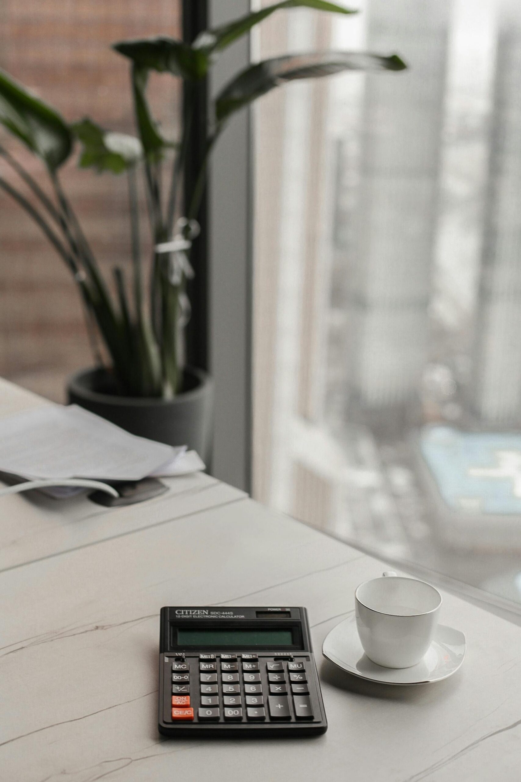 Stylish office workspace featuring a calculator and coffee cup near a large window.