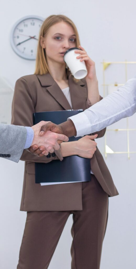 A businesswoman witnesses a professional handshake in a modern office setting.